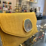 Sobre de fiesta color mostaza, hecho artesanalmente en la India, con aplique de piedra ágata a tono. Incluye asa de cadena dorada para llevar al hombro.