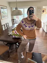 Sweater tejido a mano en mohair, de color marrón con diseño de canesú estampado con corazones fucsias y detalles geométricos en tonos beige y rosado. Presenta cuello redondo y mangas largas.