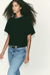 Remera negra de corte recto y holgado, con cuello redondo decorado con apliques de brillos y mangas cortas. Presenta una abertura en la espalda con cierre de botón oculto.