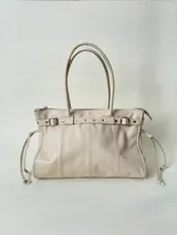 Bolso grande de cuero marrón con textura tipo cocodrilo, estructura rígida y asas para llevar al hombro. Tiene una tira con tachas y hebillas en cada extremo, también lleva lazos en los costados.