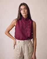 Blusa sin mangas de lino color bordó, de silueta recta y relajada, con cuello alto plisado y cartera lateral asimétrica decorada con volados tableados y botones forrados al tono.