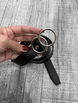 Cinto negro de cuero sintético con hebilla de doble argolla plateada.