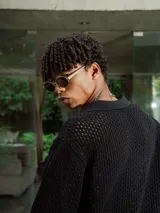 Camisa de manga corta color crudo/blanco, confeccionada en tejido de punto abierto con textura calada y cuello polo. Presenta cierre frontal de botones.