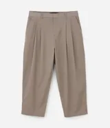 Pantalón de vestir color beige, de corte amplio estilo japonés, con cintura con trabillas, cierre tradicional, pliegues frontales, bolsillos laterales y traseros, y efecto satinado.