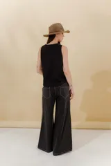 Pantalón de jean gris oscuro, estilo sastrero de tiro medio bajo y corte ancho (wide leg). Presenta costuras marcadas en el frente y un cinturón trenzado marrón con hebilla metálica.
