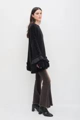 Sweater negro de lana merino con silueta amplia y relajada. Presenta mangas acampanadas con volumen, decoradas con volados de lino y terminaciones de flecos en los puños y en el ruedo.