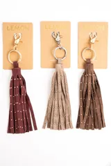 Charm para bolso compuesto por flecos de cuero sintético color marrón, decorados con pequeñas tachas metálicas doradas. Incluye un aro y un cierre de mosquetón metálico en tono dorado.