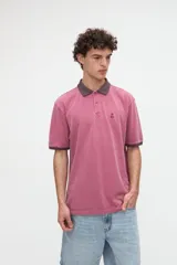 Remera polo de manga corta color rojo con efecto lavado, cuello y puños en contraste marrón. Cuenta con media cartera de botones, aberturas laterales en el dobladillo y un bordado pequeño de una estrella en el pecho.
