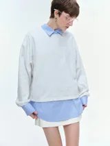 Buzo oversize de corte holgado, color gris melange, con cuello redondo acanalado y mangas largas anchas. Presenta un diseño con bajo regulable mediante elásticos.