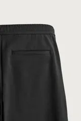 Pantalón negro confeccionado en mezcla de algodón, con cintura elástica, bolsillos frontales y cierre con cremallera y botón.