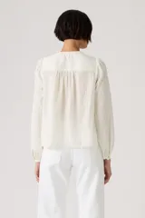 Blusa color crudo de manga larga, con cuello mao y detalles de encaje y bordados en el frente. Presenta diseño abotonado oculto y mangas abullonadas con puños elásticos.