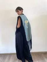 Poncho estructurado color celeste con bordado de elefante en la espalda. Presenta un diseño asimétrico, más corto adelante y largo atrás, con flecos negros que rodean toda la prenda.