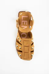 Sandalia tipo cangrejera de gamuza color camel, con diseño de tiras entrelazadas y tachas metálicas doradas. Cuenta con cierre de pulsera con hebilla ajustable y suela plana de goma.