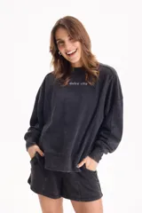 Buzo deportivo sin frisa de color negro con efecto lavado, cuello redondo, mangas largas y estampa frontal con texto en blanco.