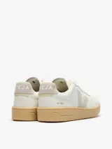 Championes Veja modelo V-90, de diseño urbano en color blanco con detalles en gris claro y suela de goma color caramelo. Presentan el logo de la marca en el lateral y perforaciones en la puntera.