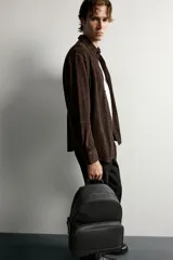 Mochila negra con acabado texturizado, compartimento principal con cierre de cremallera y bolsillo frontal con cremallera. Incluye parte posterior acolchada, asa de mano superior y dos asas de hombro ajustables.