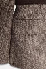 Blazer de corte sastre con estampado de espiga en tonos marrones, cuello solapa, hombreras y manga larga. Incluye bolsillos delanteros con solapa, cierre frontal con botón y un cinturón oscuro con hebilla metálica que entalla la cintura.