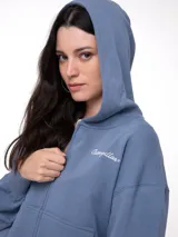 Buzo con cierre frontal completo, confeccionado en tejido french terry color azul grisáceo. Presenta diseño de corte relajado, mangas largas con puños elásticos y bordado de la marca en el pecho.