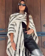 Ruana de lana merino color crudo con rayas verticales negras y flecos en el borde inferior.