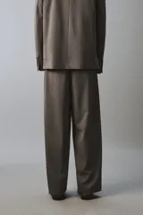 Pantalón de traje wide fit color marrón oscuro con textura, pinzas frontales, bolsillos laterales y cierre con cremallera y botón.