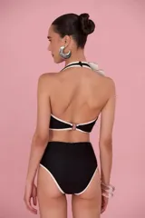 Malla enteriza negra con ribetes blancos, diseño halter con escote profundo y aberturas laterales en la cintura. Presenta un aplique de flor tridimensional en el tirante derecho.