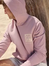 Buzo con capucha color lila, de algodón y fit relajado. Presenta un estampado con una palmera y el texto "Rainbow Bay" en el pecho.