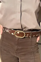 Cinturón de cuero con textura de pelo vacuno, estampado animal print tipo bambi en tonos marrón y blanco, con hebilla ovalada de metal envejecido.