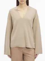 Sweater color beige de lana con escote en v, mangas largas y hombros caídos. Presenta logo de Calvin Klein en la parte superior trasera.