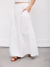 Falda larga blanca de diseño fluido con paneles horizontales fruncidos, cintura elástica con cordón de ajuste y bolsillos laterales.