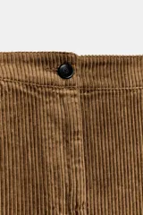 Pantalón de tiro medio confeccionado en tejido de pana, con diseño de pierna ancha, bolsillos delanteros y traseros, y cierre frontal con cremallera y botón.