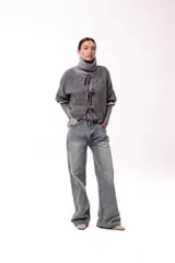 Saco de punto gris con frente abierto, cierre mediante lazos frontales y mangas con puños elásticos. Presenta una textura suave y un diseño de volumen holgado.