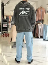 Canguro oversize gris con efecto acid wash, capucha y gran estampado blanco en la espalda con tipografía y estrella estilizada.