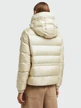 Campera puffer Moncler modelo Biron, color beige perlado, con capucha integrada, cierre frontal y bolsillos laterales con cierre. Presenta diseño acolchado horizontal y logo de la marca en la manga.