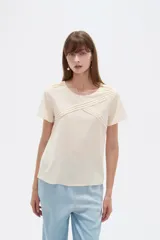 Blusa de viscosa color natural, con cuello a la base, manga corta y detalle de plisado cruzado en el frente. Presenta un corte holgado.
