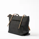 Bolso tipo shopper de tela color gris oscuro con textura, asas de cuero color beige y detalle de borla decorativa.