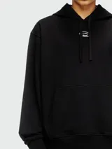 Buzo negro con capucha de corte holgado, con logo metálico en el pecho y bolsillo tipo canguro.