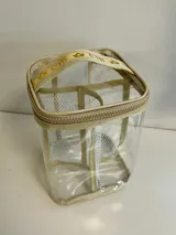 Necessaire transparente de PVC con bordes y asa en tela color beige, cierre superior con cremallera.