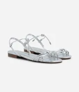 Sandalia plana marca Satinato, color dorado metalizado con textura tipo croco. Posee tiras finas con detalle de nudo en el empeine y cierre de lazo ajustable al tobillo. Diseño de puntera redonda y suela plana.