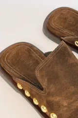 Sueco de gamuza color marrón con detalle de tachas metálicas doradas alrededor de la suela y punta redonda.