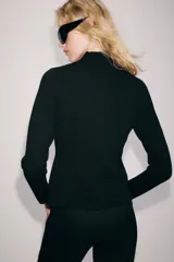 Chaqueta de punto negro con escote en V y manga larga. Cierre frontal con una hilera de pequeños botones forrados.