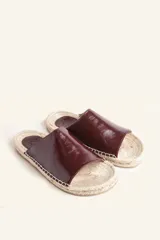 Sandalias tipo alpargata con capellada de cuero charol color bordó y planta tejida en fibra natural de yute. Presentan costuras a mano en color blanco y suela de goma.