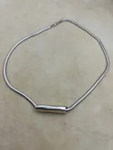 Gargantilla plateada con cadena de eslabones tipo serpiente y dije cilíndrico horizontal.