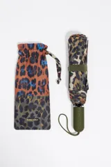 Paraguas plegable con funda de tela estampada en patrón patchwork de leopardo, combinando tonos verde oliva, terracota y negro, con detalles en azul. El mango es de goma color verde oliva con la marca grabada.