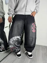Jeans baggy negro de corte ancho, con efecto lavado, detalle de bordado de flores de cerezo en la parte superior y gran estampado inspirado en la gran ola en la parte inferior de la pierna.