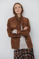 Chaqueta de gamuza en tono marrón oscuro, con cuello alto, cierre frontal con cremallera y botones a presión, bolsillos frontales con solapa y cinturón ajustable en la cintura.