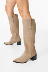 Bota bucanera de cuero color marrón oscuro, con taco cuadrado de 6 cm y punta fina con detalle metálico. Presenta una tira vertical decorativa con tachas metálicas en la parte superior de la caña.