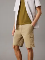Shorts cargo color beige confeccionados en sarga de algodón elástico, de corte recto y talle medio. Cuenta con cierre de botón y cremallera, cintura elástica en los laterales, bolsillos con ranura en los laterales, bolsillos traseros ribeteados y bolsillos cargo.