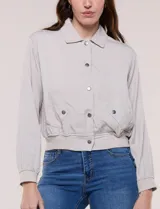 Camperita bomber de lyocell con textura suave, color azul marino, cuello camisero, cierre frontal con botones a presión, bolsillos laterales con solapa, mangas largas con puños elásticos y pretina fruncida en el ruedo.