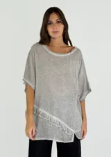 Blusa gris de lino y algodón, de corte amplio, con cuello redondo y mangas cortas con terminación desflecada. Presenta un volante diagonal en el frente.