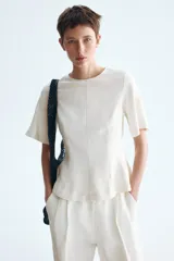 Blusa blanca de manga corta con escote redondo, costuras moldeadoras y diseño peplum acampanado con cierre trasero de botón.